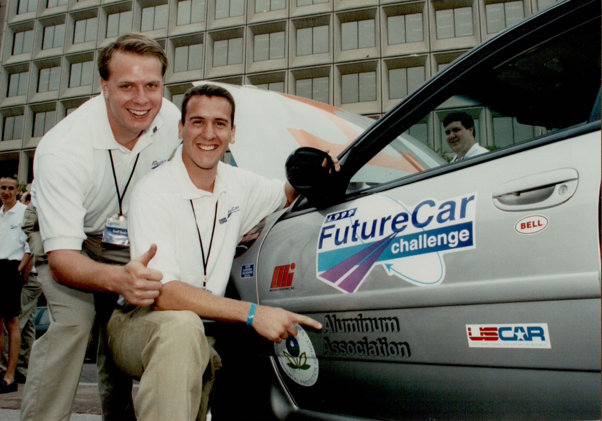 Two men standing by a car door pointing to a logo that says "Aluminum Association"